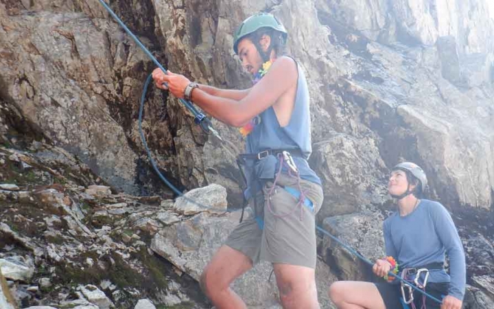 a gap year student belays a climber while another looks on during the rock climbing portion of an outdoor educator course with outward bound